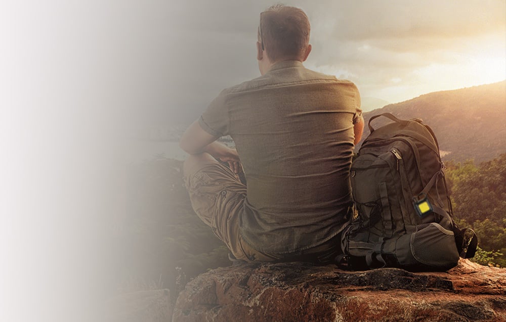 A man sitting on a rock with a backpack and a small lamp attached to it