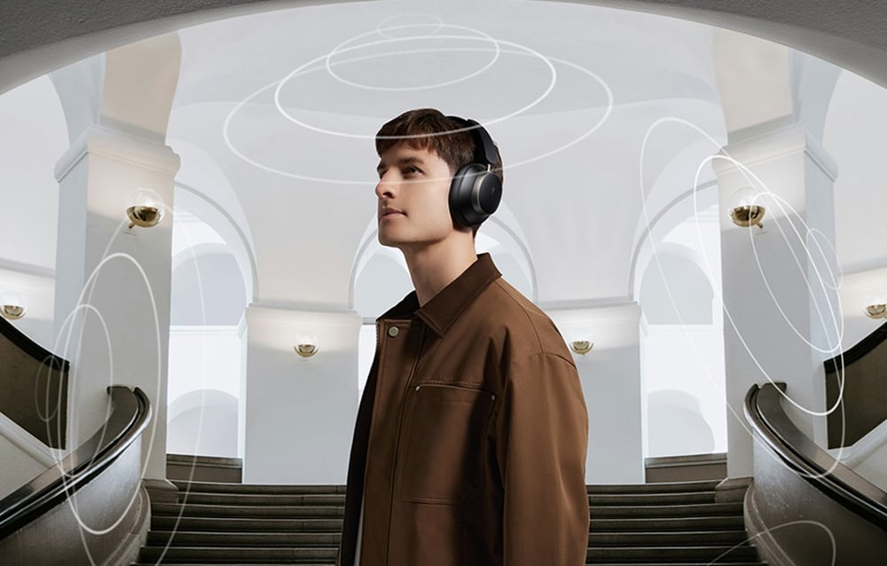 A man in a brown jacket wearing headphones stands in front of the stairs