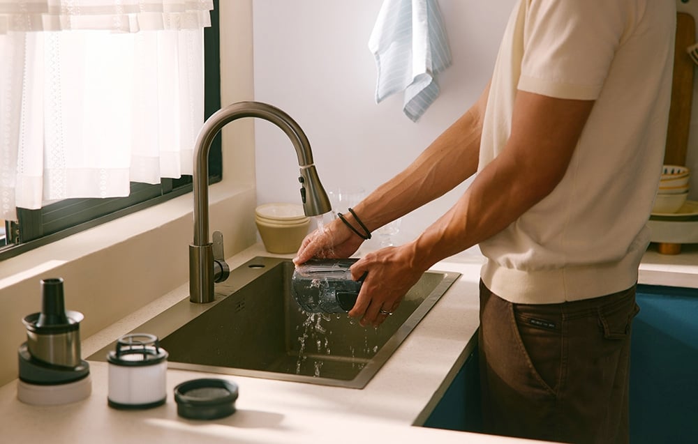 Mężczyzna myje pod bieżącą wodą w zlewie kuchennym pojemnik od odkurzacza bezprzewodowego.