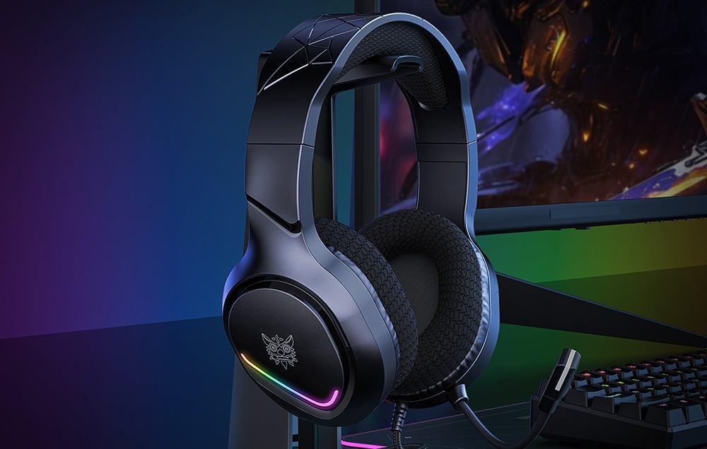 Gray headphones with colorful backlight on a stand next to the keyboard and monitor