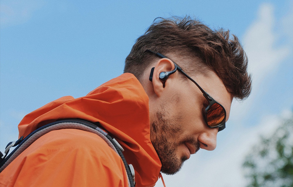 A man in an orange jacket, with glasses and an earpiece in his ear