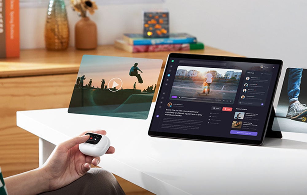 A person holds a case with headphones in front of a tablet that is playing multimedia content