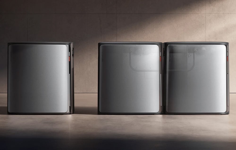 Three silver energy storage units stacked side by side on the floor against a brown wall