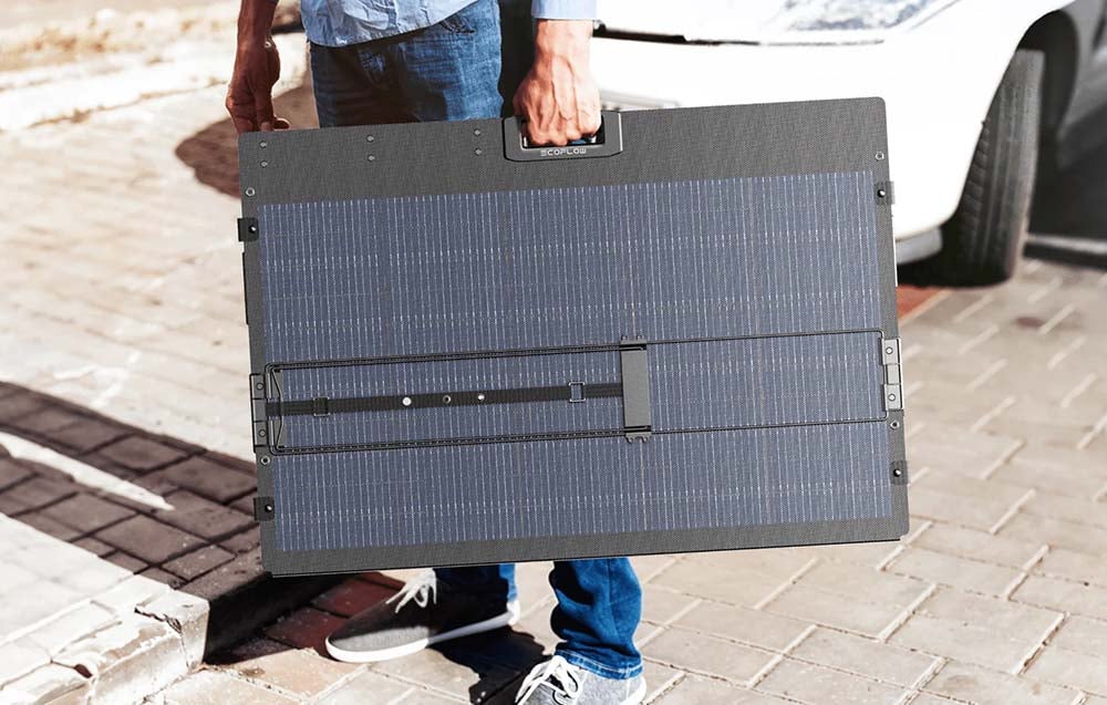 Person holding a folded portable photovoltaic panel with a handle in the middle