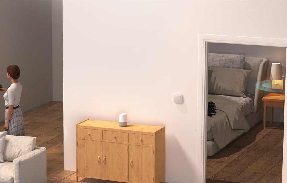 A woman in the living room overlooking the bedroom, where the bedside lamp is controlled automatically