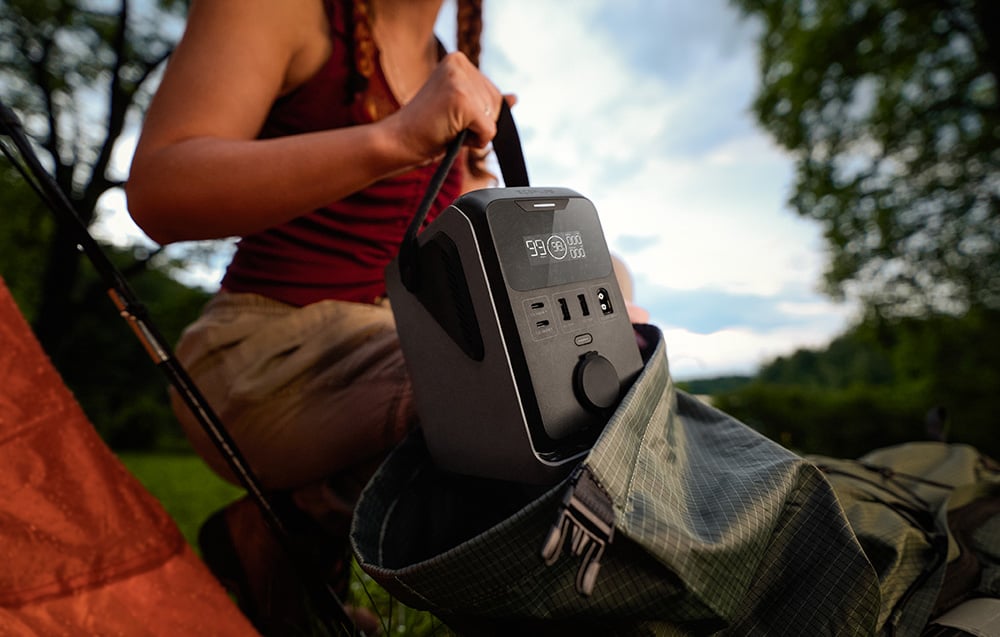 A woman puts a portable power station into a hiking backpack in the woods