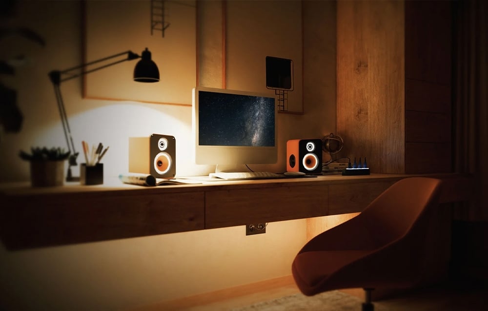 A sleek desk in a darkened room with a computer, speakers, lighting and a modern chair - a stylish workspace