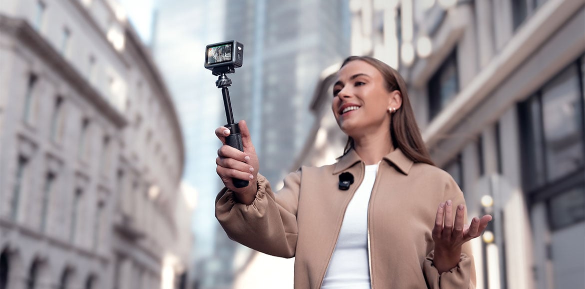 Kobieta nagrywająca vloga w mieście za pomocą małej kamery na wysięgniku