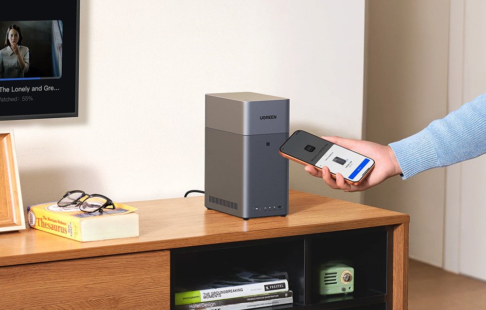 Hand with phone over UGREEN NAS server on the cabinet, TV and books in the background
