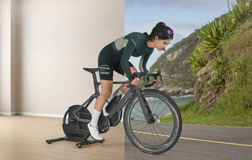 Woman training on a bike with a trainer next to a landscape projected on the wall