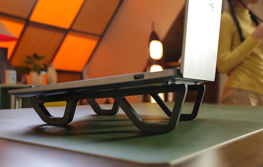 Laptop stoi na biurku na czarnym, niskim stojaku o geometrycznym kształcie