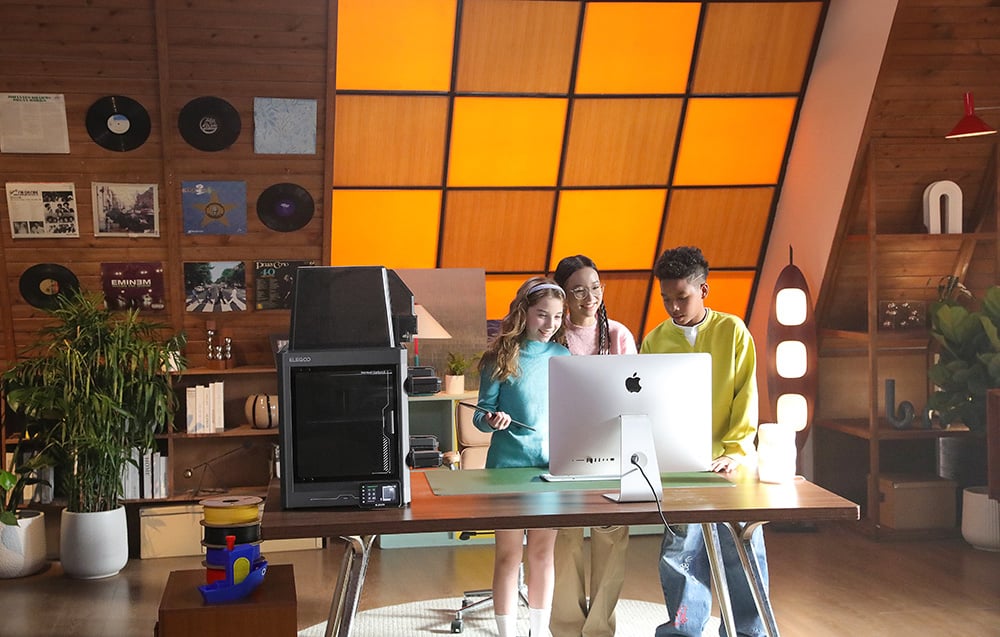Troje dzieci stoi przy biurku z komputerem i drukarką 3D w przytulnym pomieszczeniu z drewnianymi ścianami
