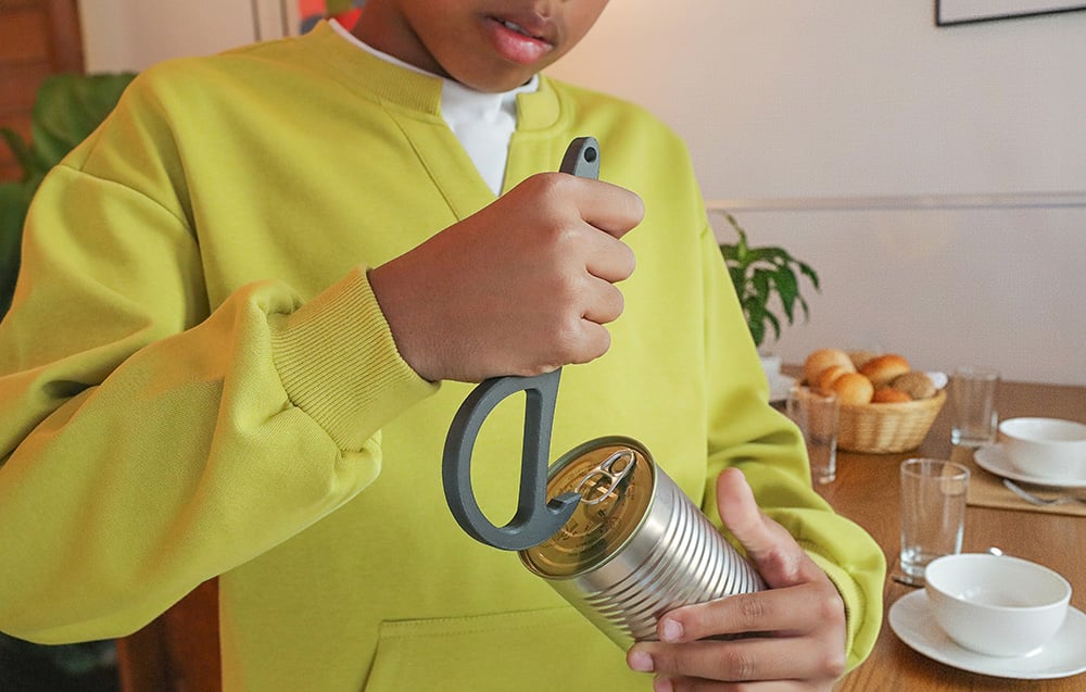 Chłopiec w zielonej bluzie używa czarnego uchwytu do otwarcia puszki z napojem lub jedzeniem