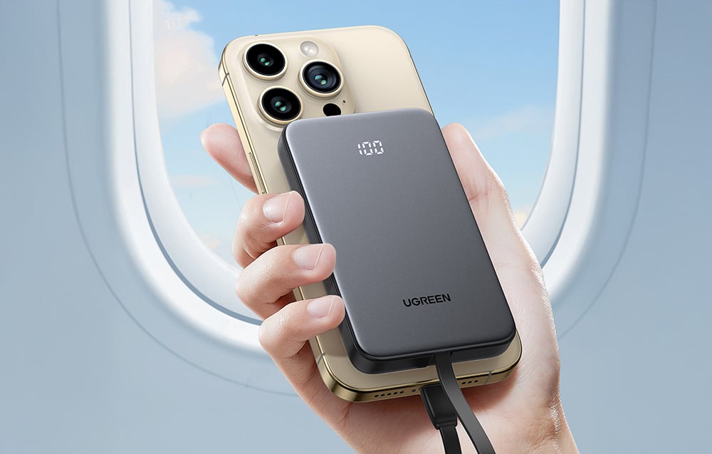 Kéz, amely egy okostelefonhoz csatlakoztatott power bankot tart egy repülőgép ablakának hátterében.