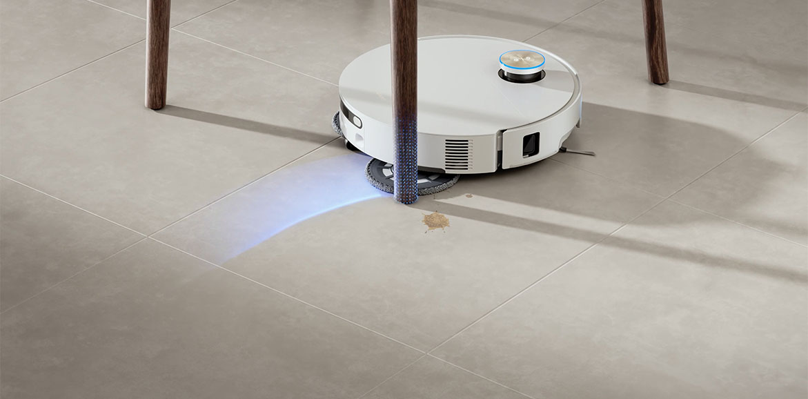 Biały robot sprzątający odkurza przestrzeń pod krzesłem