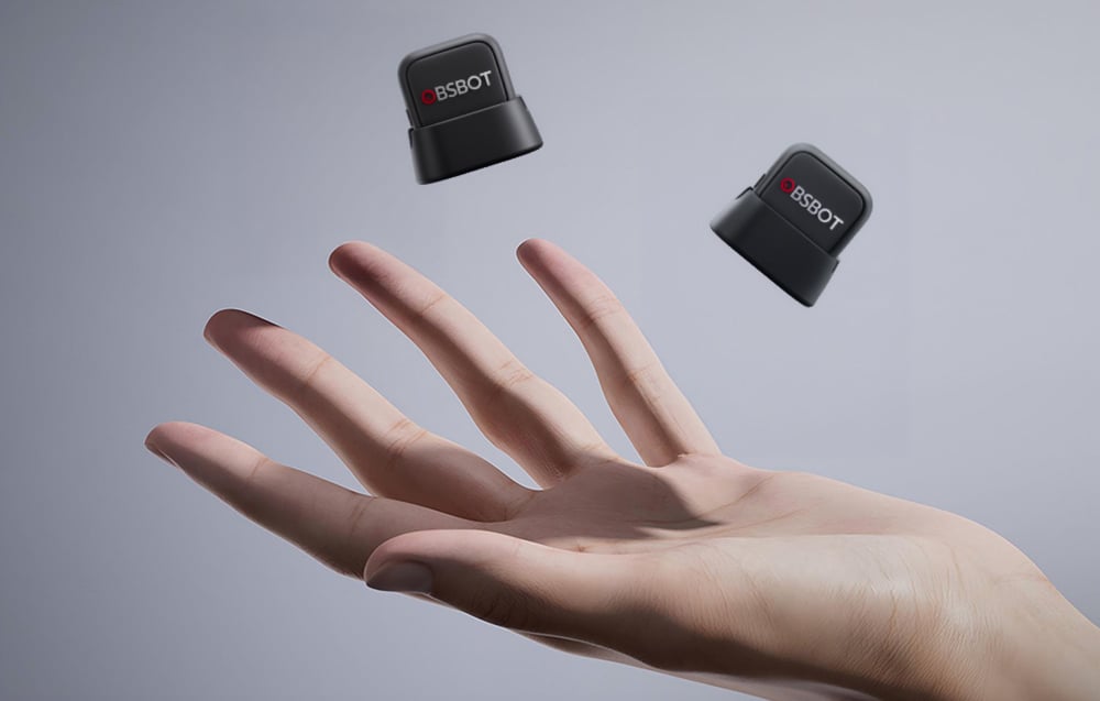 Two compact OBSBOT microphones hovering over an open hand, showing off the minimalist design with the distinctive red logo