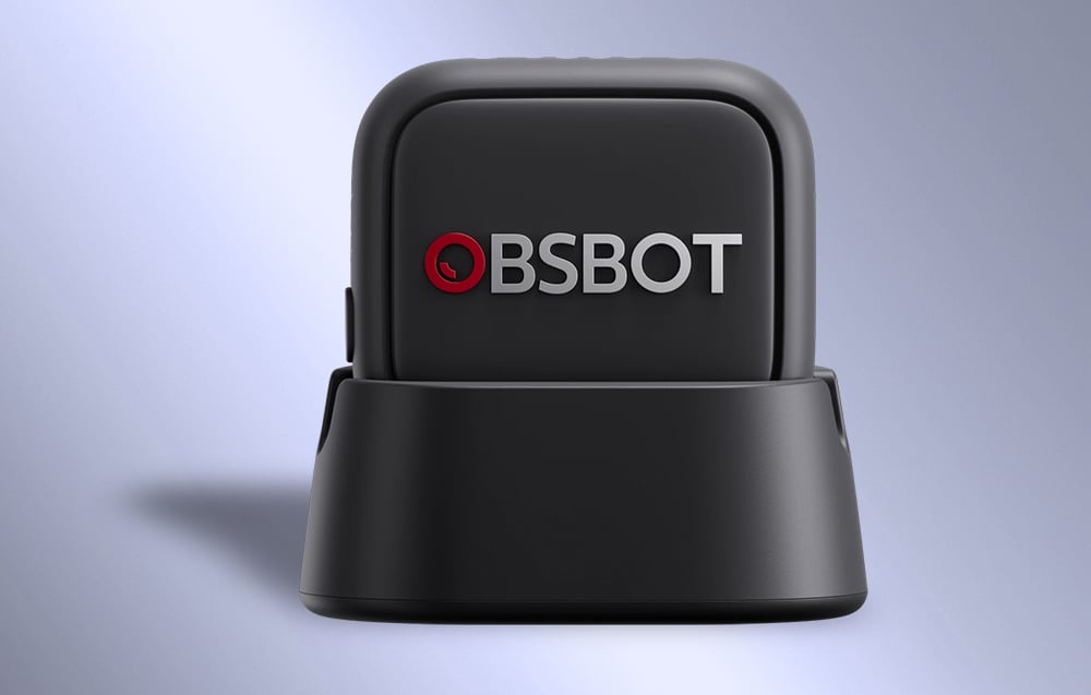 Mikrofon OBSBOT w czarnej obudowie umieszczony na ładującej podstawie z widocznym logo na przednim panelu