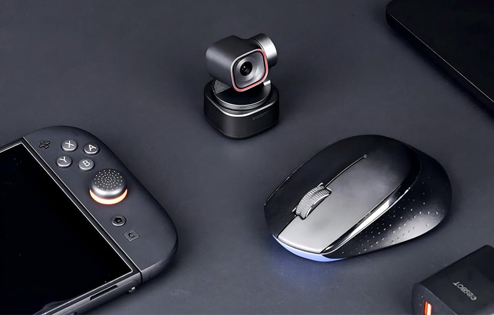 Kamera OBSBOT na obrotowej podstawie umieszczona na biurku obok pilota zdalnego sterowania i myszki komputerowej