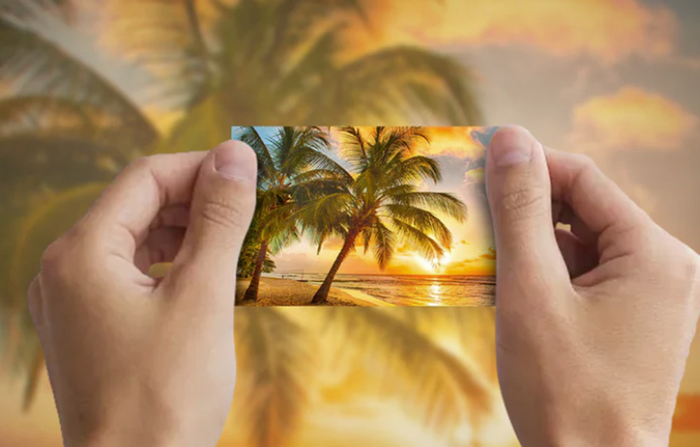 Hands holding a photo with palm trees and a sunset