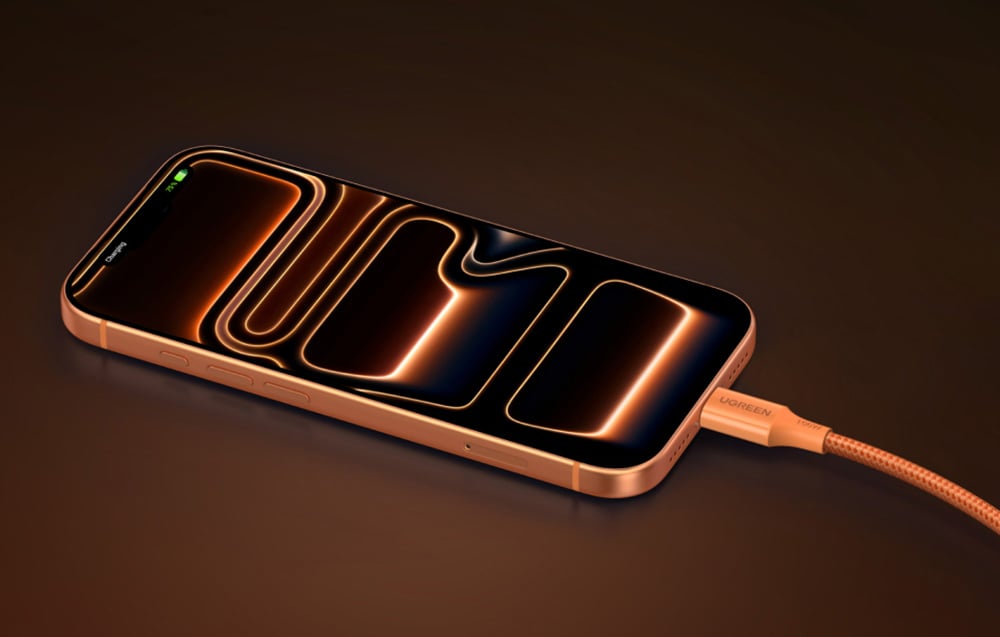 A smartphone charged with an orange UGREEN cable lies on a surface with a dark background.