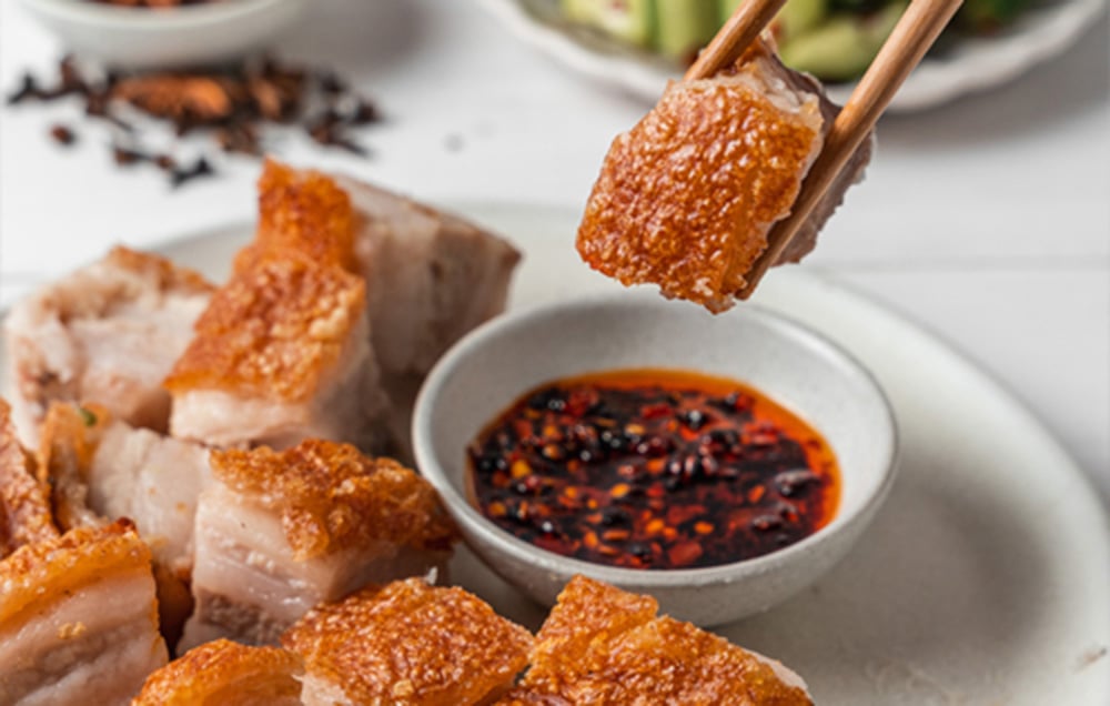 Chrupiący kawałek pieczonego boczku unosi się nad miseczką z sosem