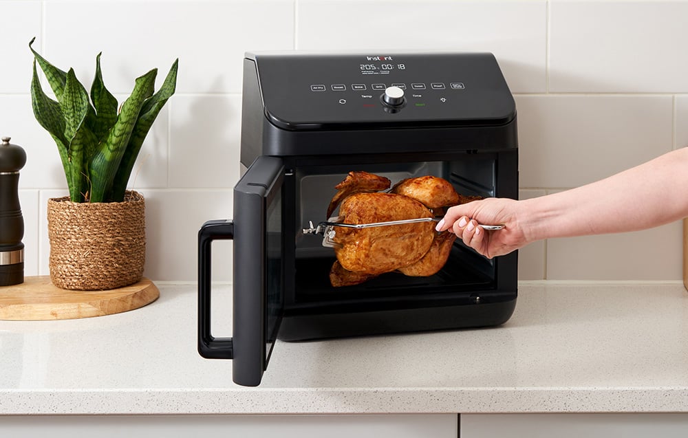 Ręka wsuwa pieczonego kurczaka na rożnie do otwartego czarnego piekarnika