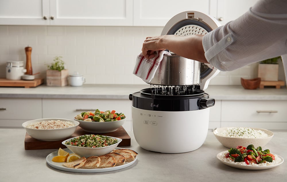 Ociekający wodą metalowy wkład jest wyciągany z ryżowaru w otoczeniu gotowych dań