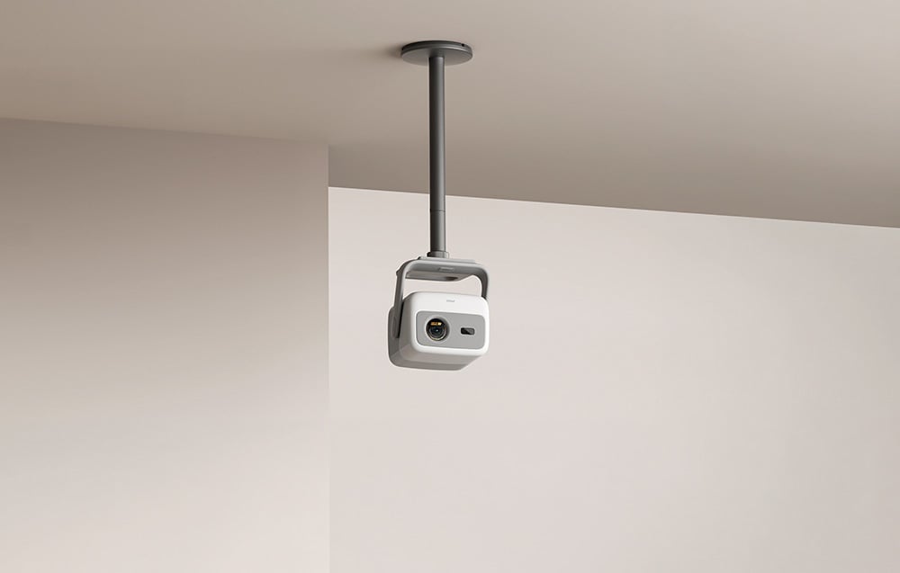 A projector on a ceiling mount directed toward a light-colored wall in a modern interior.