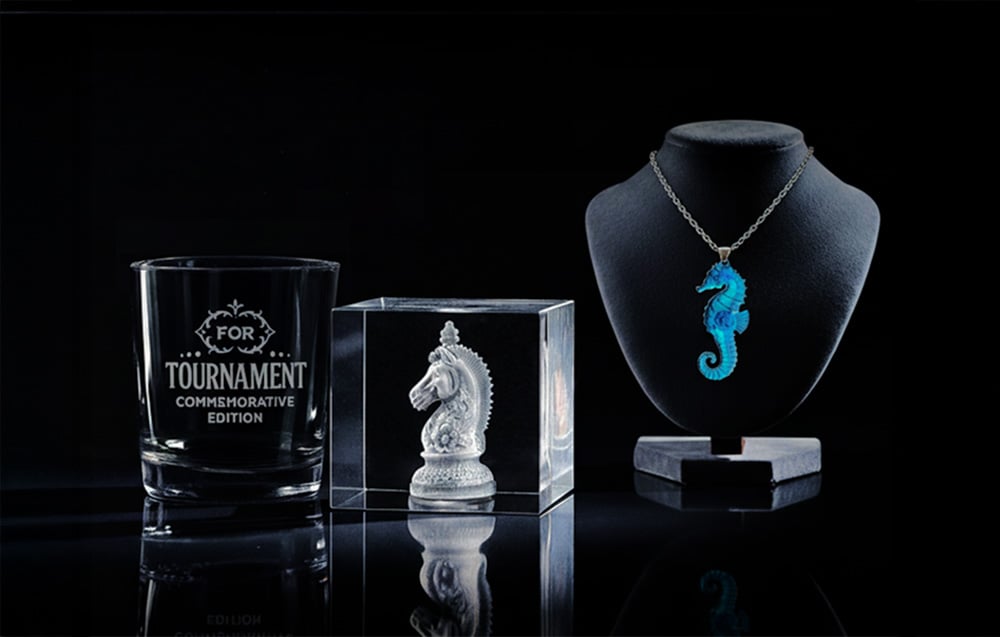 Three items with engraving: a glass with an inscription, a glass cube with a horse figure and a blue pendant in the shape of a seahorse