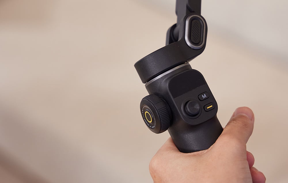 Hand holding a black gimbal - close-up of the control panel with a dial and buttons.