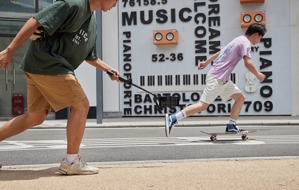 A man uses a gimbal to film someone skateboarding on a city street.