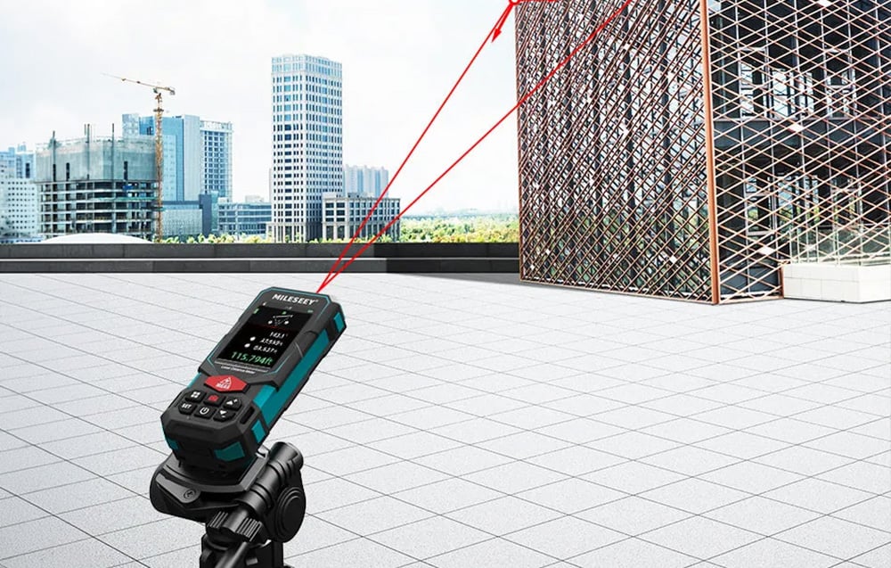 Laser rangefinder on a tripod, measuring the distance to a metal building structure.
