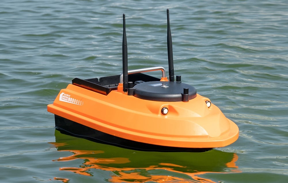An orange bait boat floating peacefully on the surface of clear water on a sunny day.