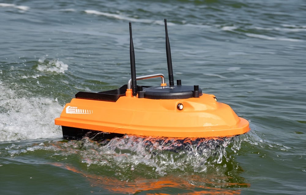 A bait boat sailing on the water, creating waves and splashes around the hull.