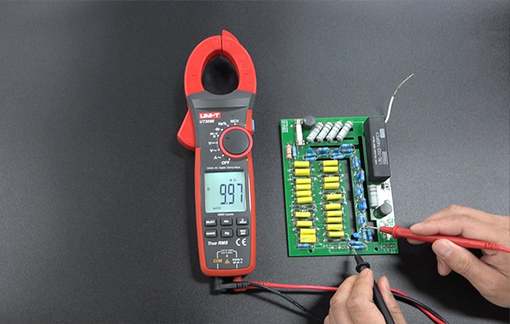UNI-T meter on a black countertop measuring components on a green PCB.