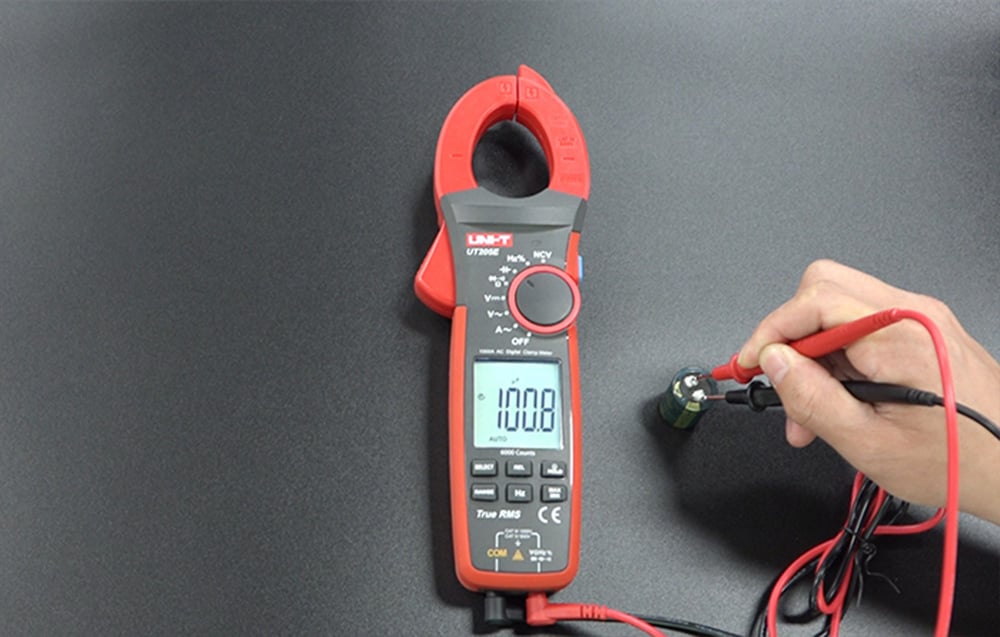UNI-T digital meter next to a cylindrical capacitor under test on a dark surface.