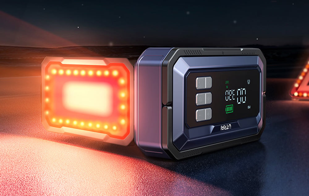 A car jump starter lying on the road with a red warning light on.