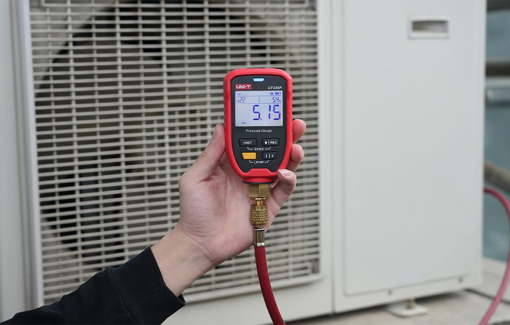 Elektroniczny manometr UNI-T podczas pomiaru ciśnienia w zewnętrznej jednostce klimatyzatora.