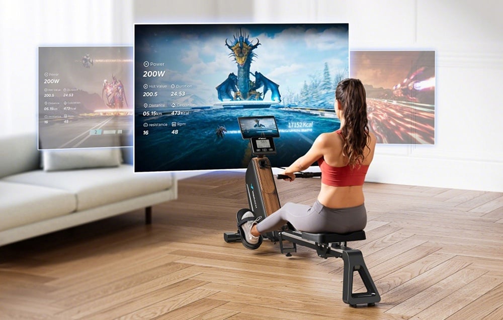 A woman exercises on a rowing machine in the living room, watching an interactive game displayed on a large screen in front of her
