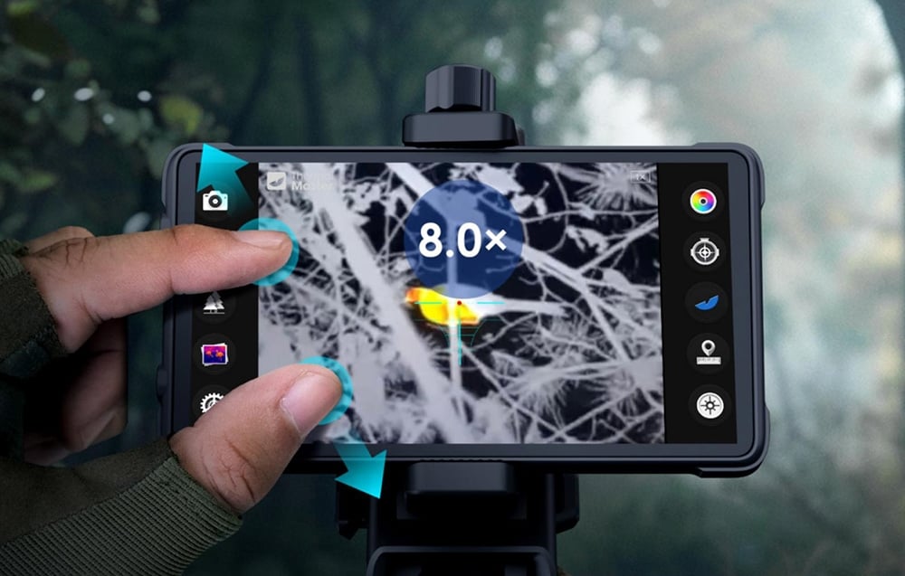 Fingers zoom in on the phone screen to reveal a thermal, warm-colored image of a bird sitting on a branch.