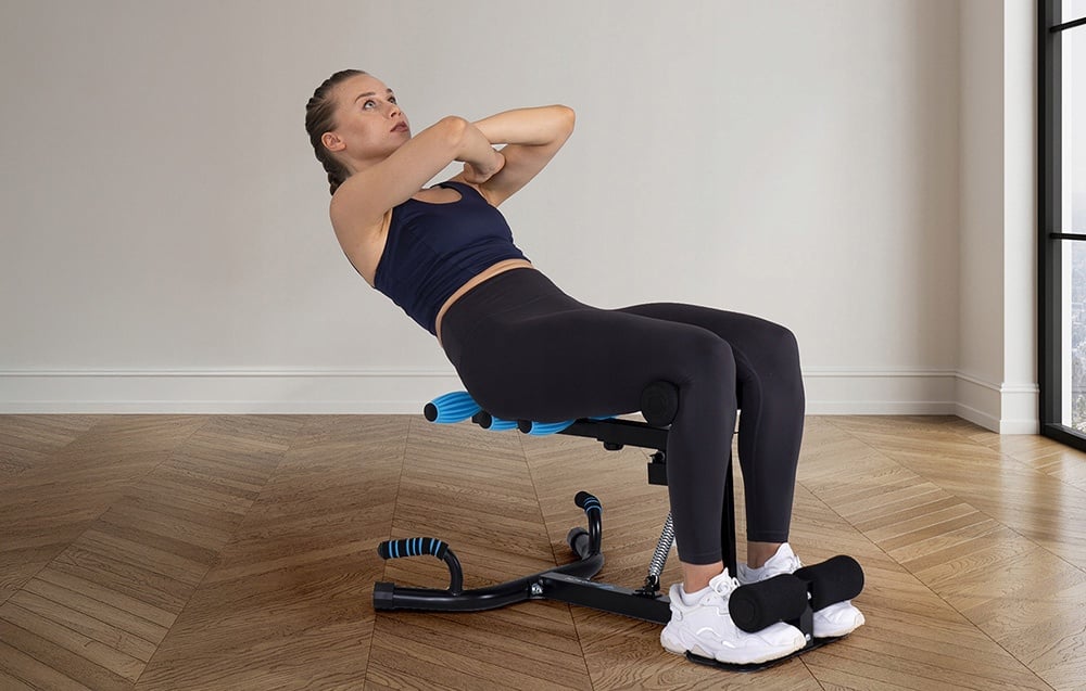 A woman in dark workout clothes performs a back bend on a workout bench with blue rollers