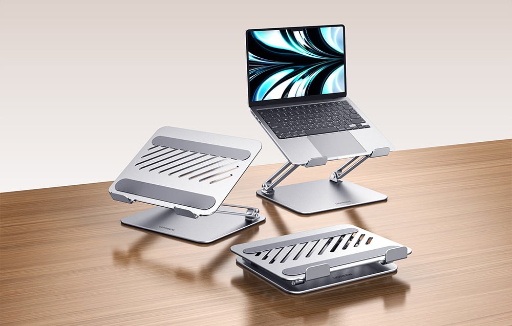 Három fém laptopállvány – az egyiken laptop, a másik kettő üres – egy fa asztallapon