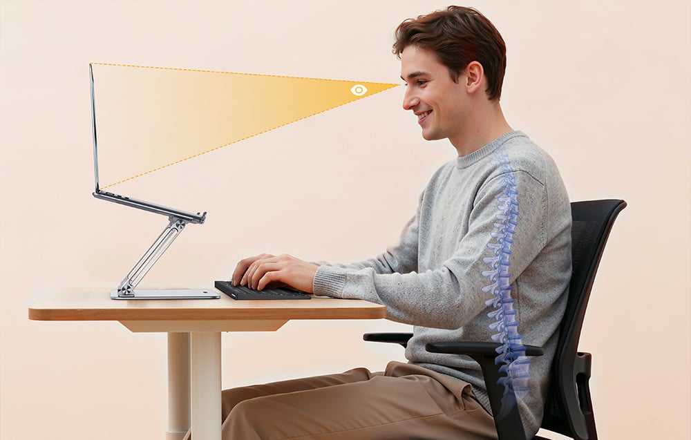 Egy férfi ül az íróasztalnál, és egy állítható állványon elhelyezett laptopot néz