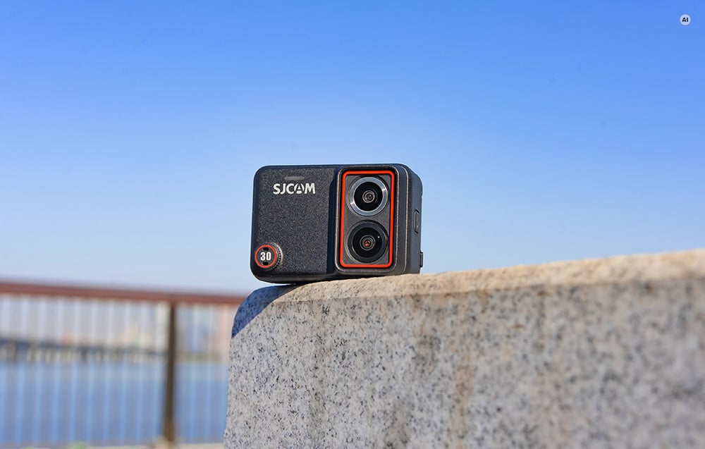 Egy SJCAM kettős lencsés akciókamera, amely egy alacsony falon nyugszik kék égbolt előtt.
