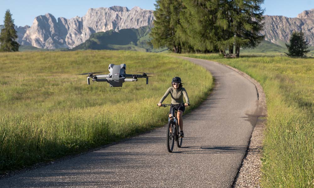 Dron nagrywający kobietę jadącą na rowerze po ścieżce na tle gór